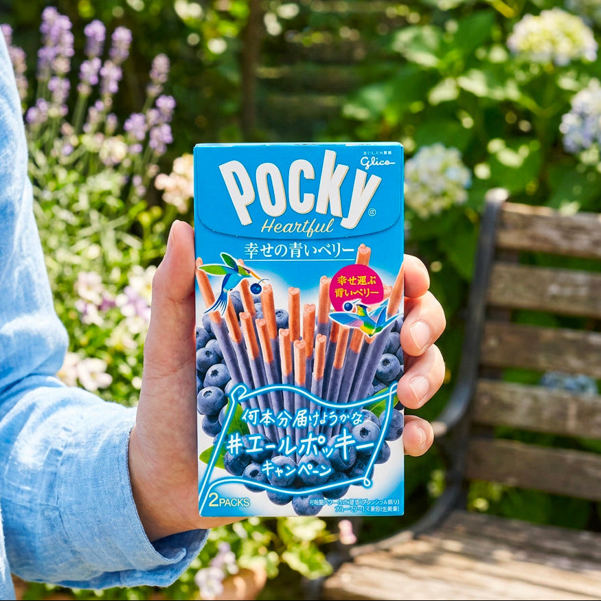 Dans un jardin, une personne présente de sa main gauche le paquet de bâtonnets chocolatés, Glico Pocky Heartful Blueberry – disponible sur My American Shop